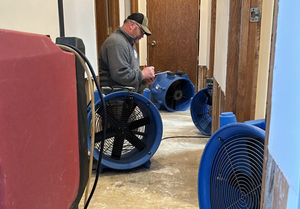 Recoveron technician checking moisture readings next to drying fans