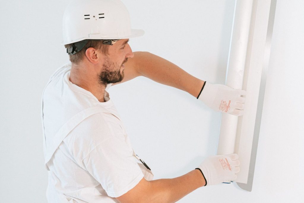 Worker in gloves fitting a new sheet of drywall
