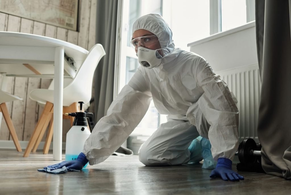 Technician in a protective suit, mask and gloves cleaning and disinfecting a floor
